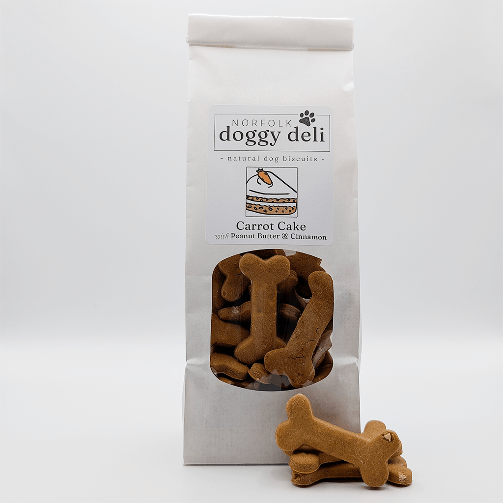 Bag of Norfolk Doggy Deli Carrot Cake dog biscuits with a single biscuit in front on a white background