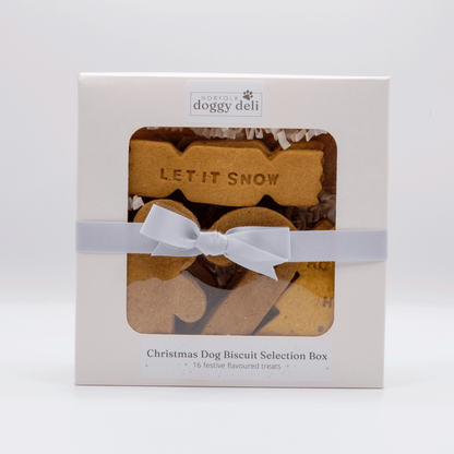 Norfolk Doggy Deli Christmas Dog Biscuit Selection Box, featuring a white box with a clear window showing assorted dog biscuits, wrapped with a white ribbon bow.